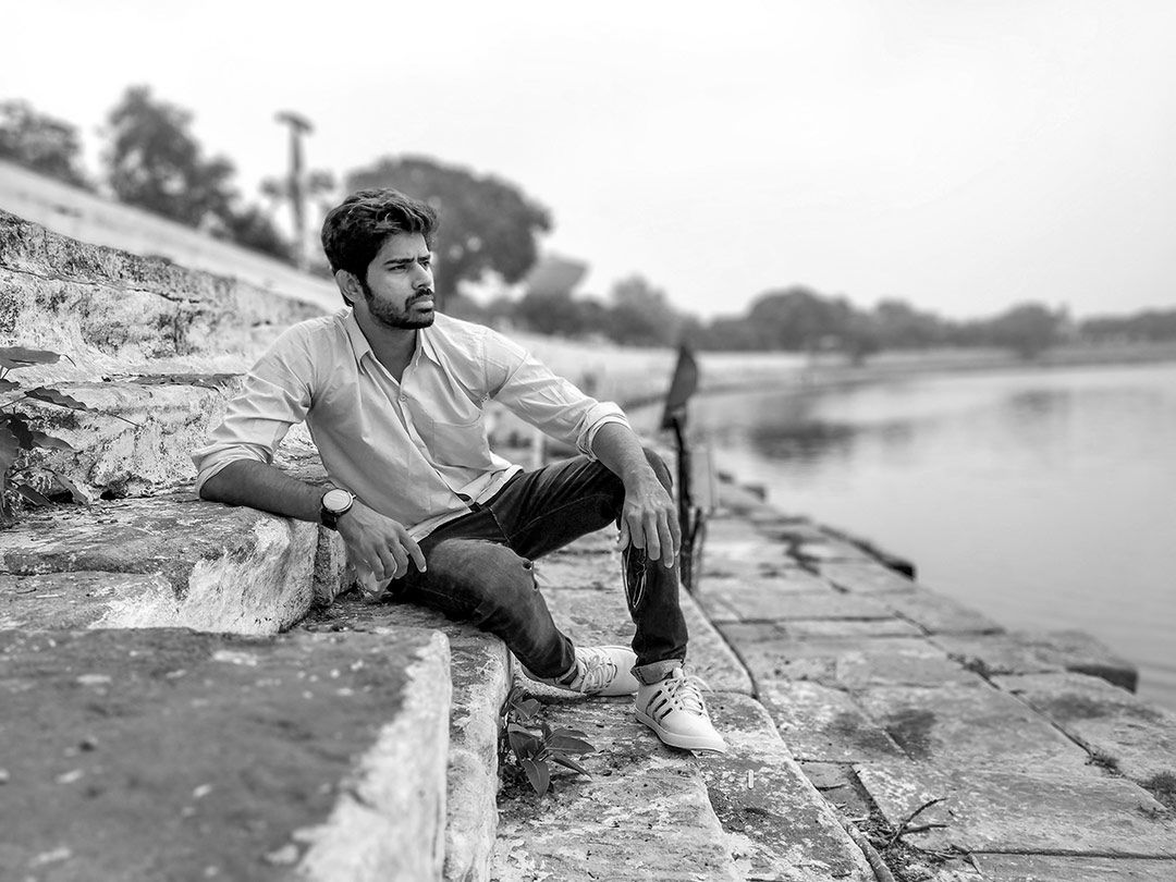 black and white image of ishaan sitting beside a river looking contemplative