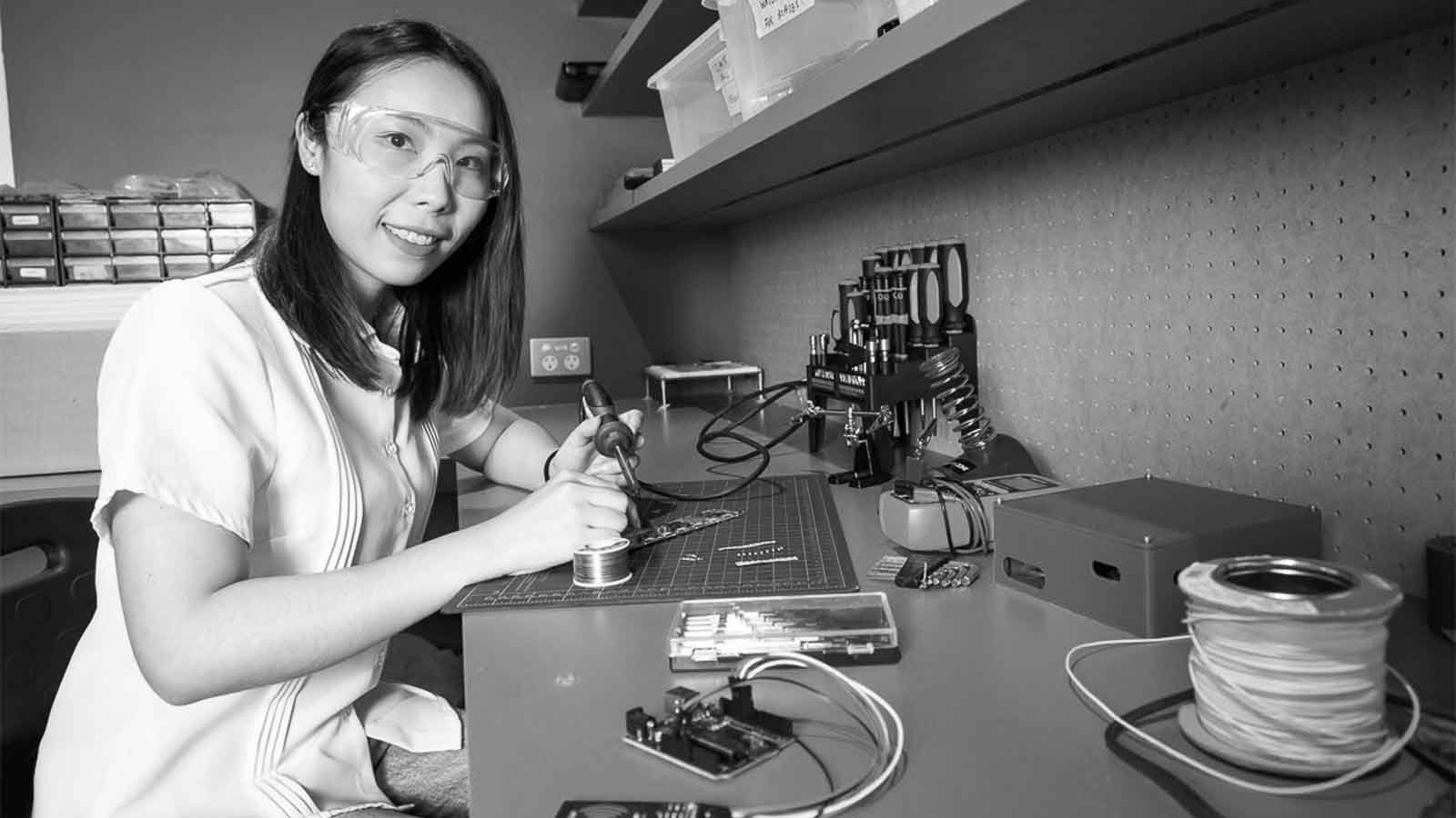 black and white image of jie li pan holding soldering equipment in a lab setting