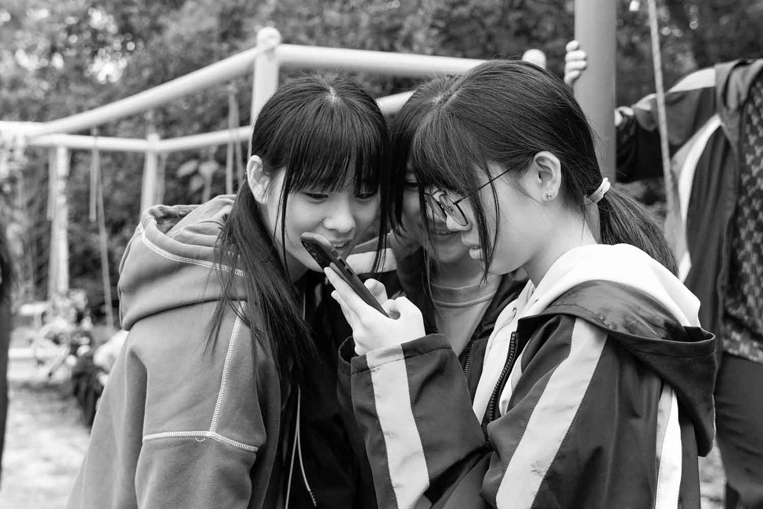 black and white image of three females holding one phone reading it closely