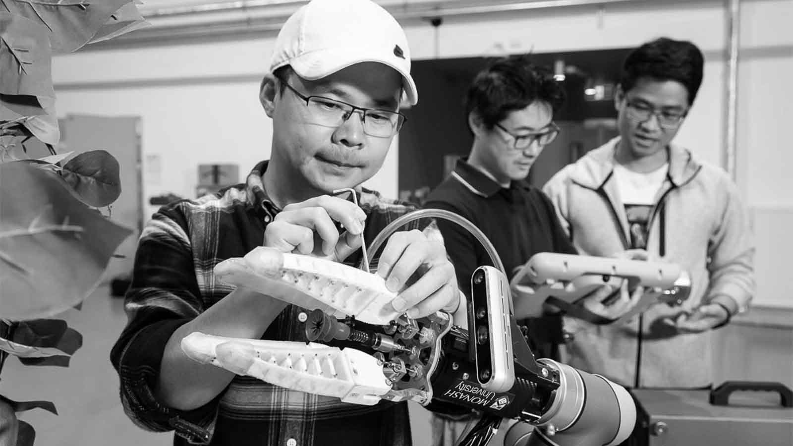 black and white image of a group of three people working closely together holding up robotic equipment