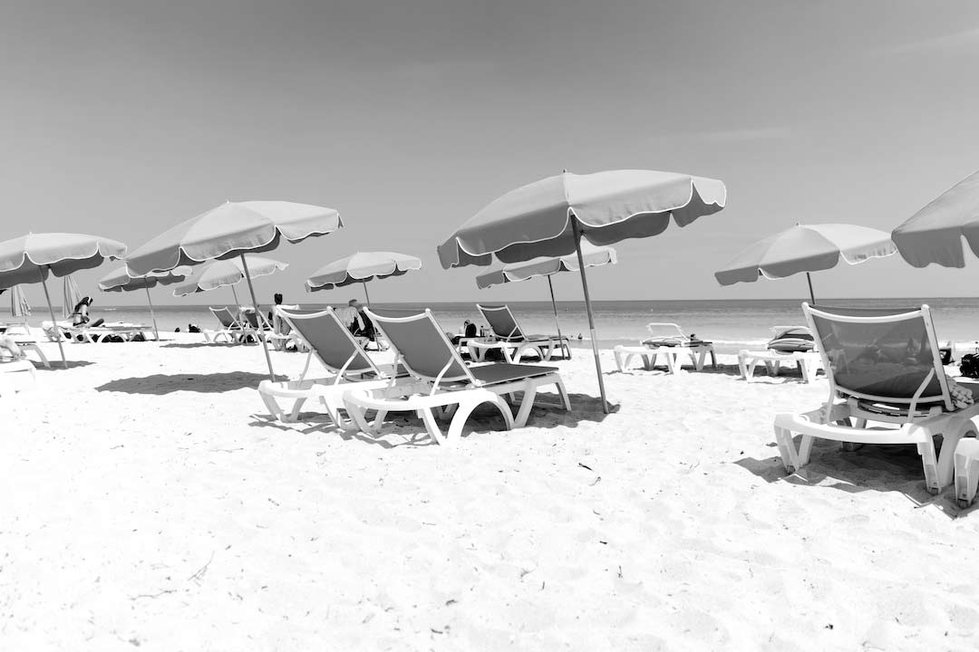 black and white photo of beach with beach deck chairs and umbrellas in groups