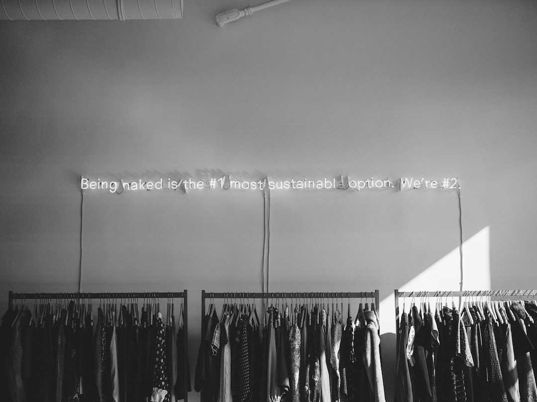 black and white image of neon lights on a fashion shop wall reading 'being naked is the 1 most sustainable fashion. we are 2'