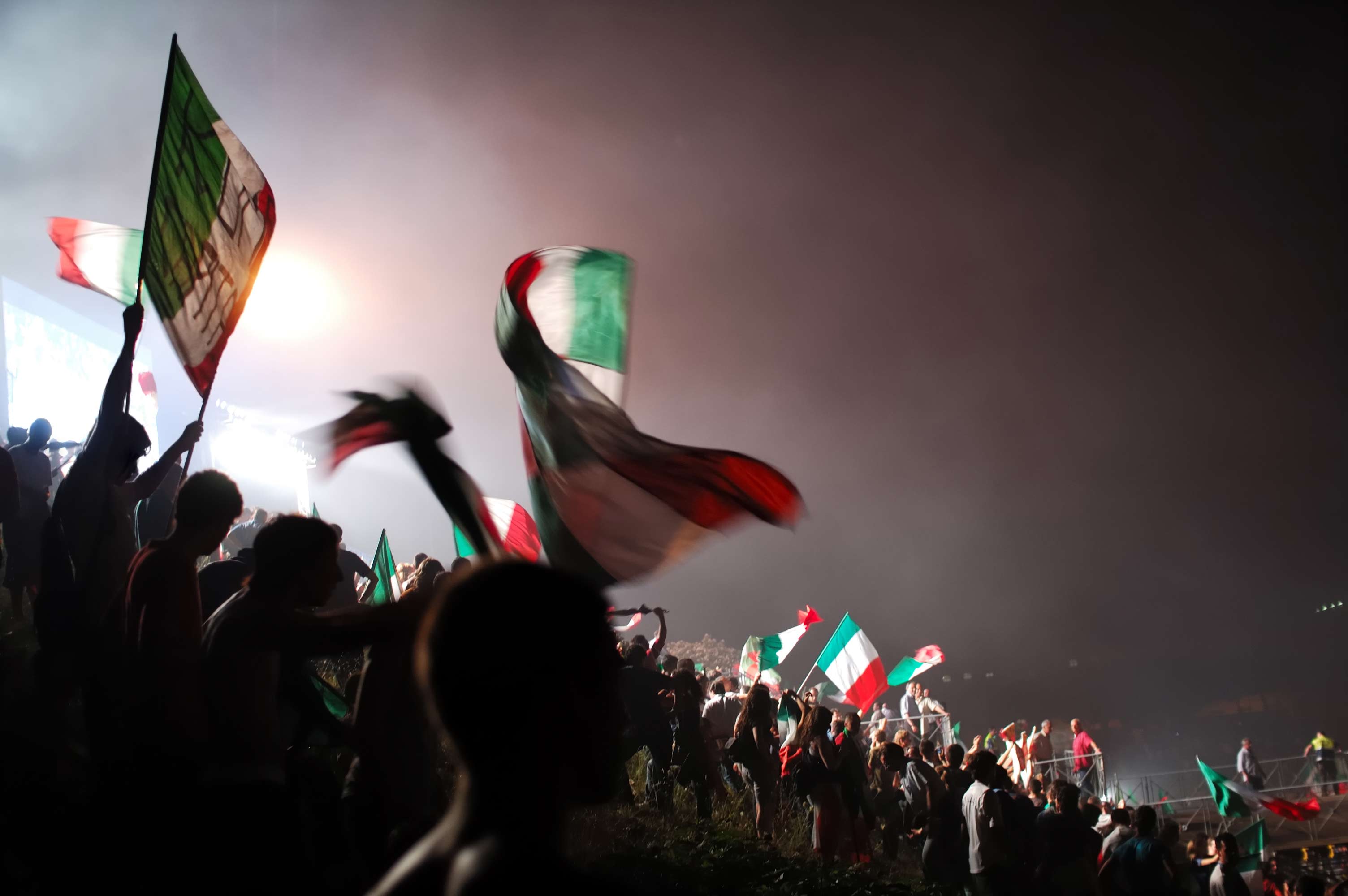 crowd of Italy supporters waving italian flags against the night sky