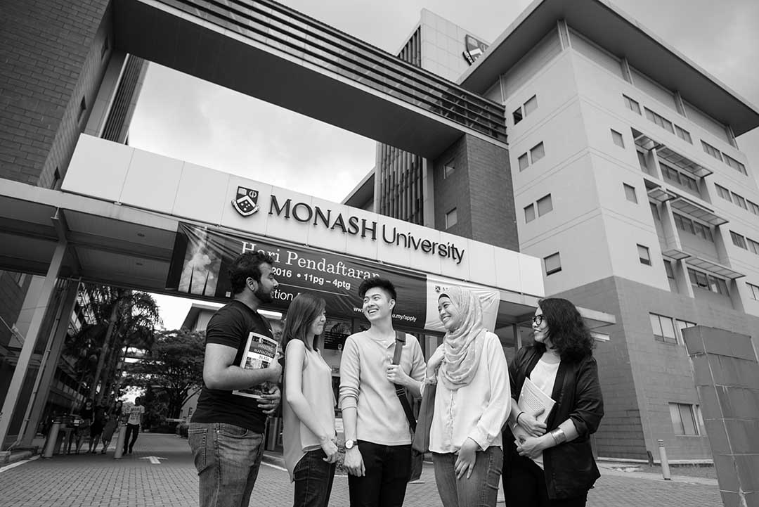 black and white image of a group of five people smiling outside a monash university building