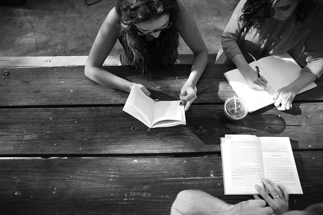 black and white image top down of a group of three people writing on notepads together on a wooden table