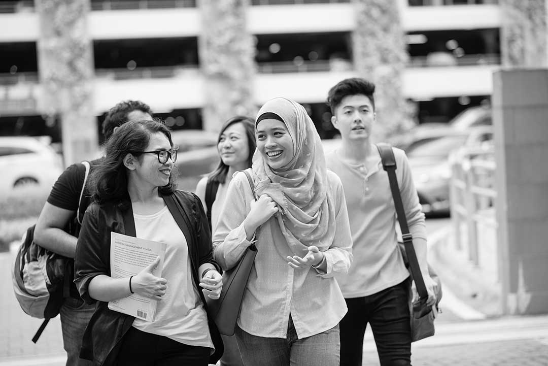 black and white image of group of friends walking towards a building smiling holding notebooks and bags