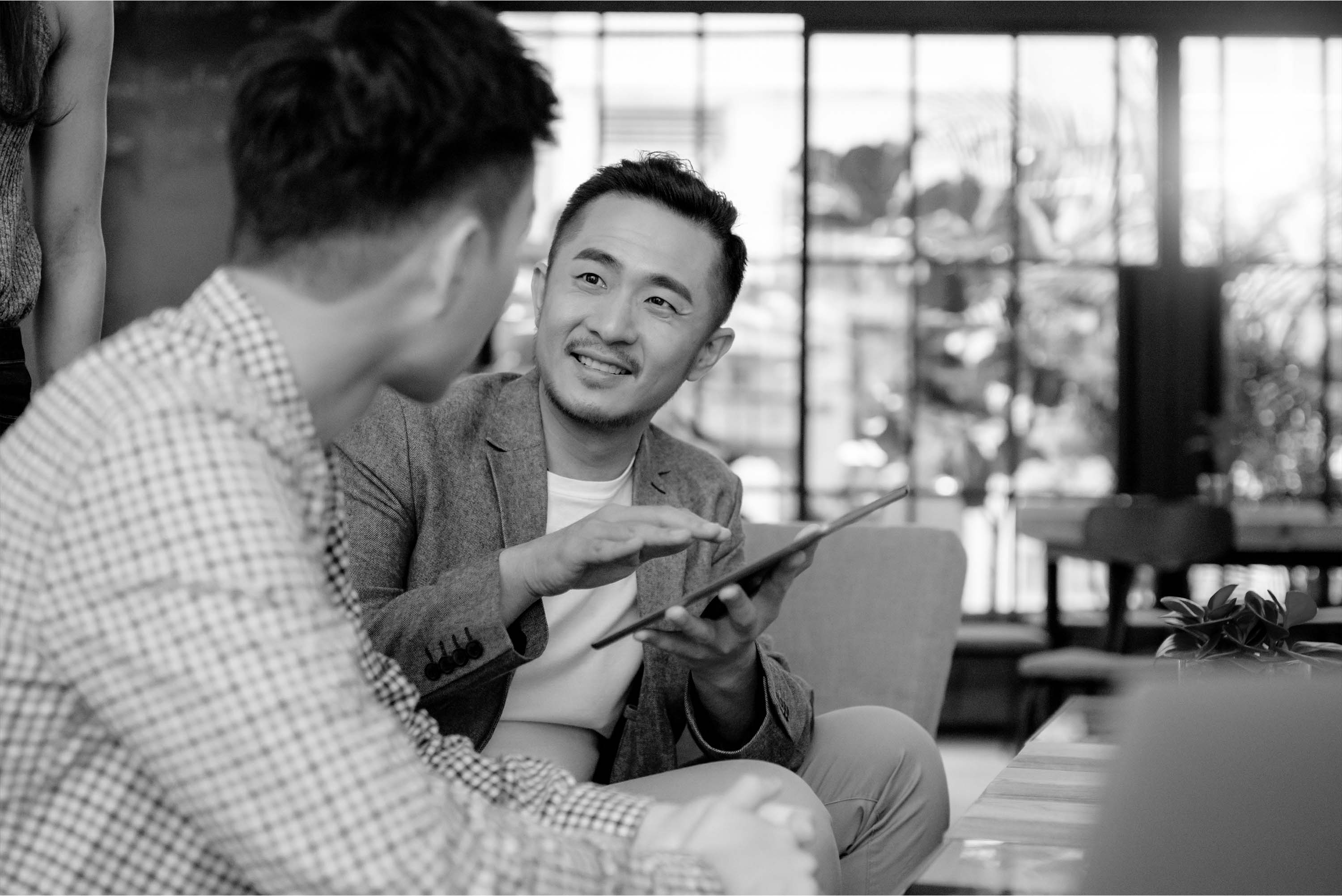 black and white image of a man sitting mentoring someone holding an ipad