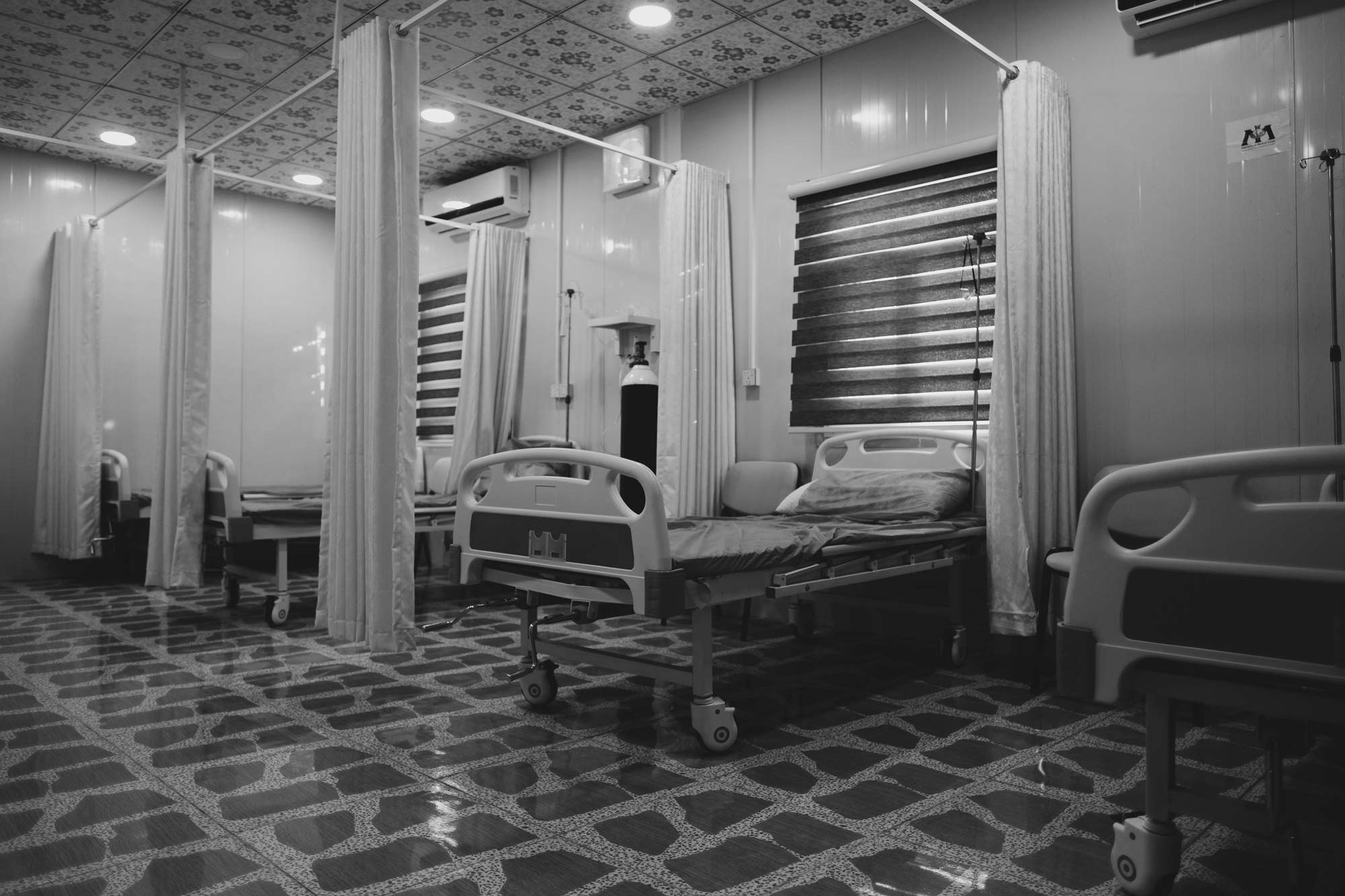 black and white image of an empty hospital room with 4 beds in it