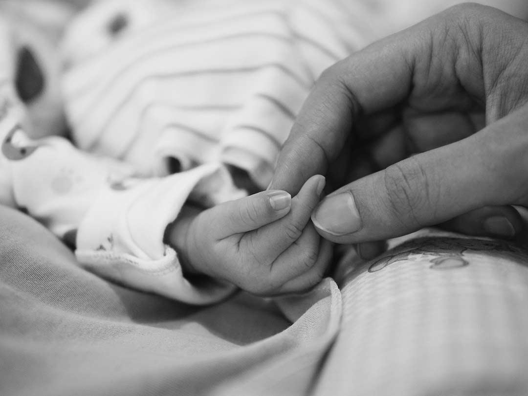 black and white image of a small baby holding a parents hand