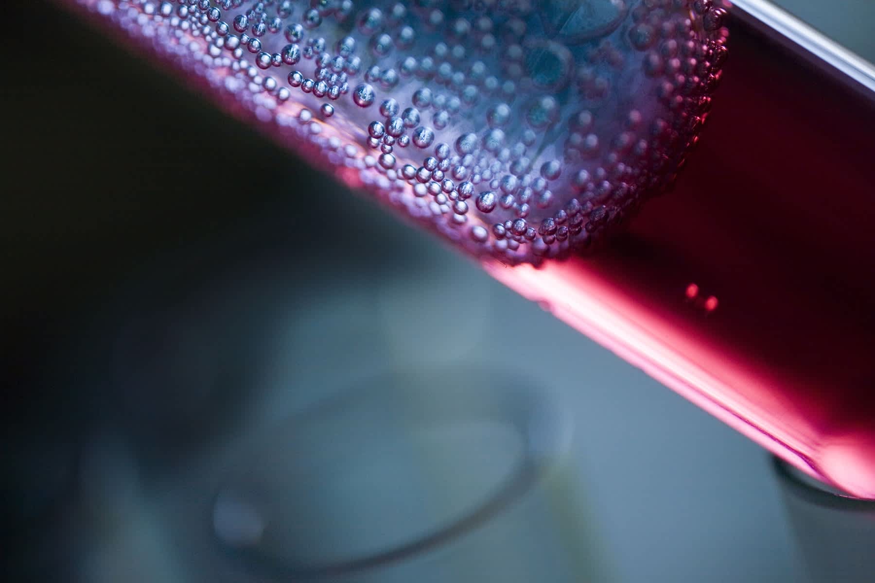 An extreme closeup of part of a syringe with red, blood-like liquid in it and moisture droplets on the outside.