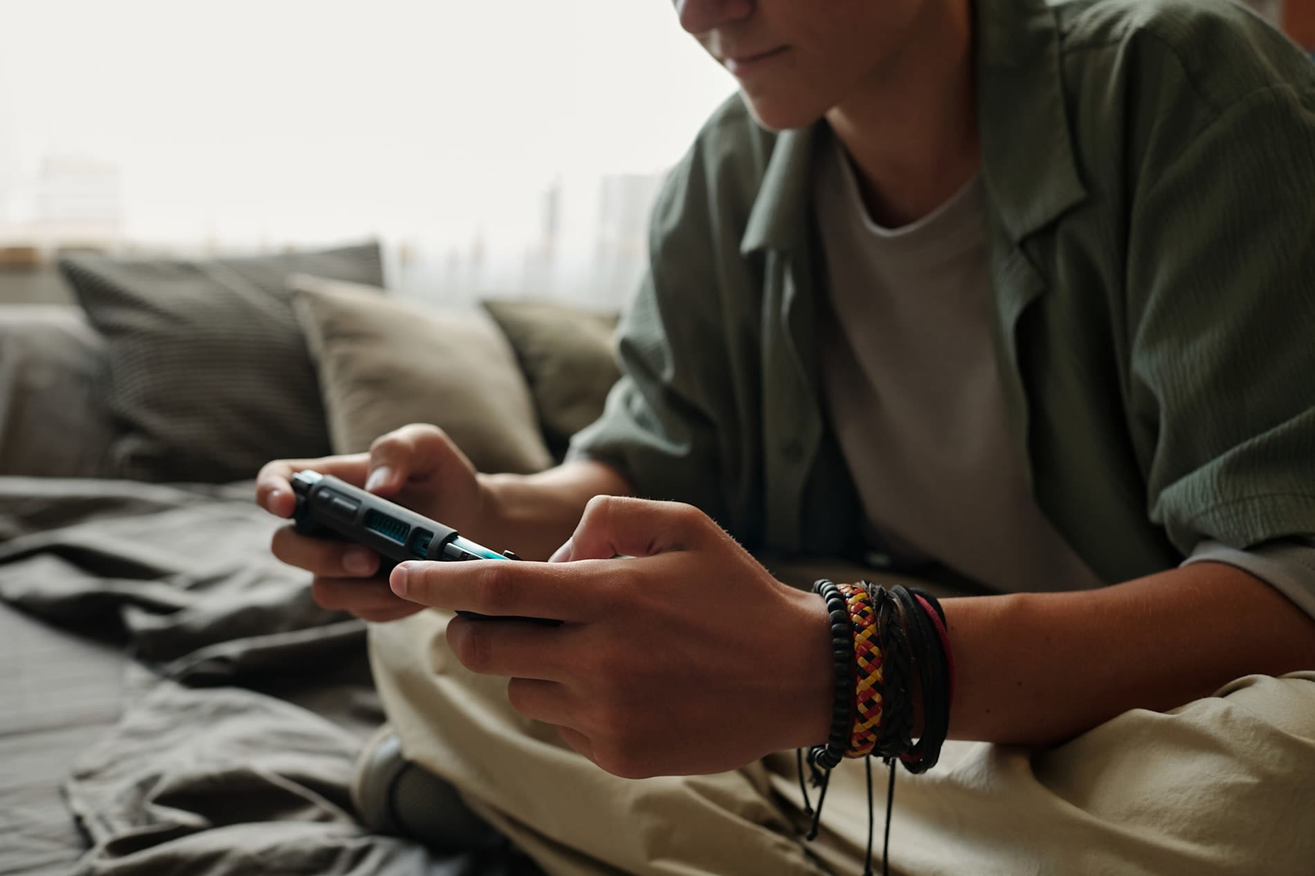 A young man wearing bracelets holds a mobile phone with both hands.