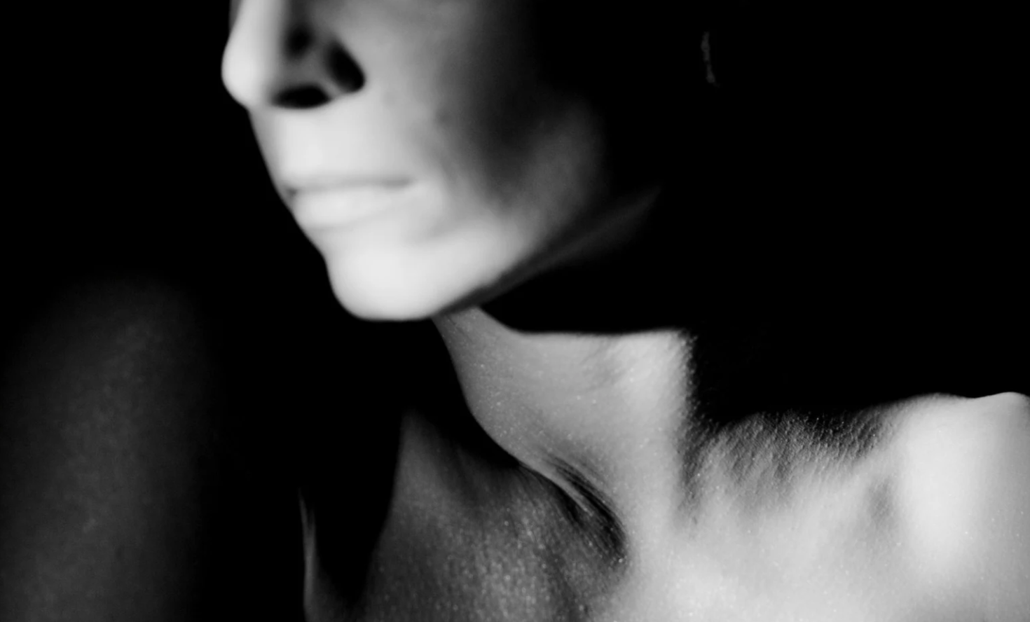 A moody, black-and-white closeup of a woman's lower face, neck and upper chest.