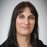 Associate Professor Bridget Harris has long dark hair. She is wearing a dark blouse and smiling in front of a plain grey background.